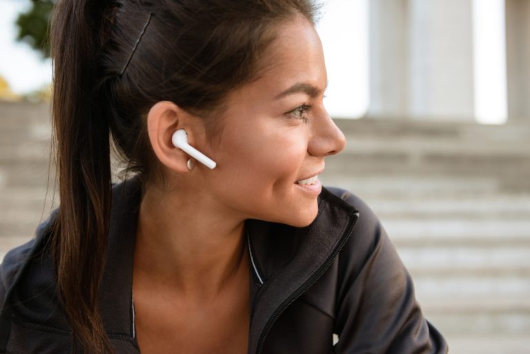 Close up portrait of a smiling fitness woman in earphones looking away while sitting outdoors